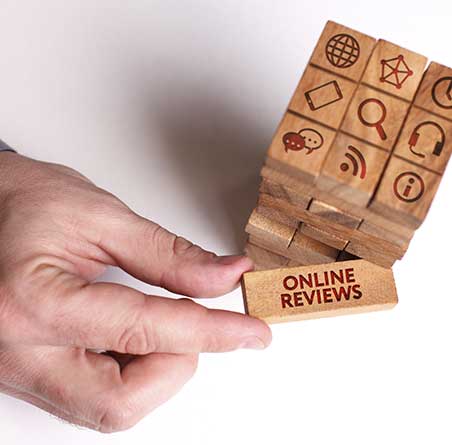 A hand pulls a tumble tower of blocks with a text review printed on the block. Tumbling tower blocks with printed icons related to website browsing